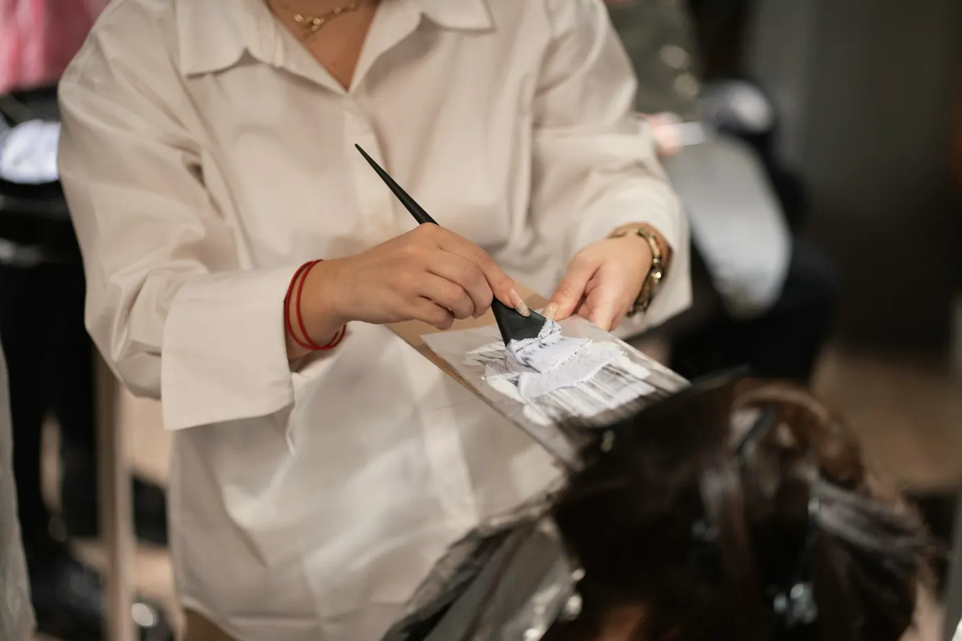Mãos aplicando coloração com pincel e papel-alumínio numa mecha de cabelo.